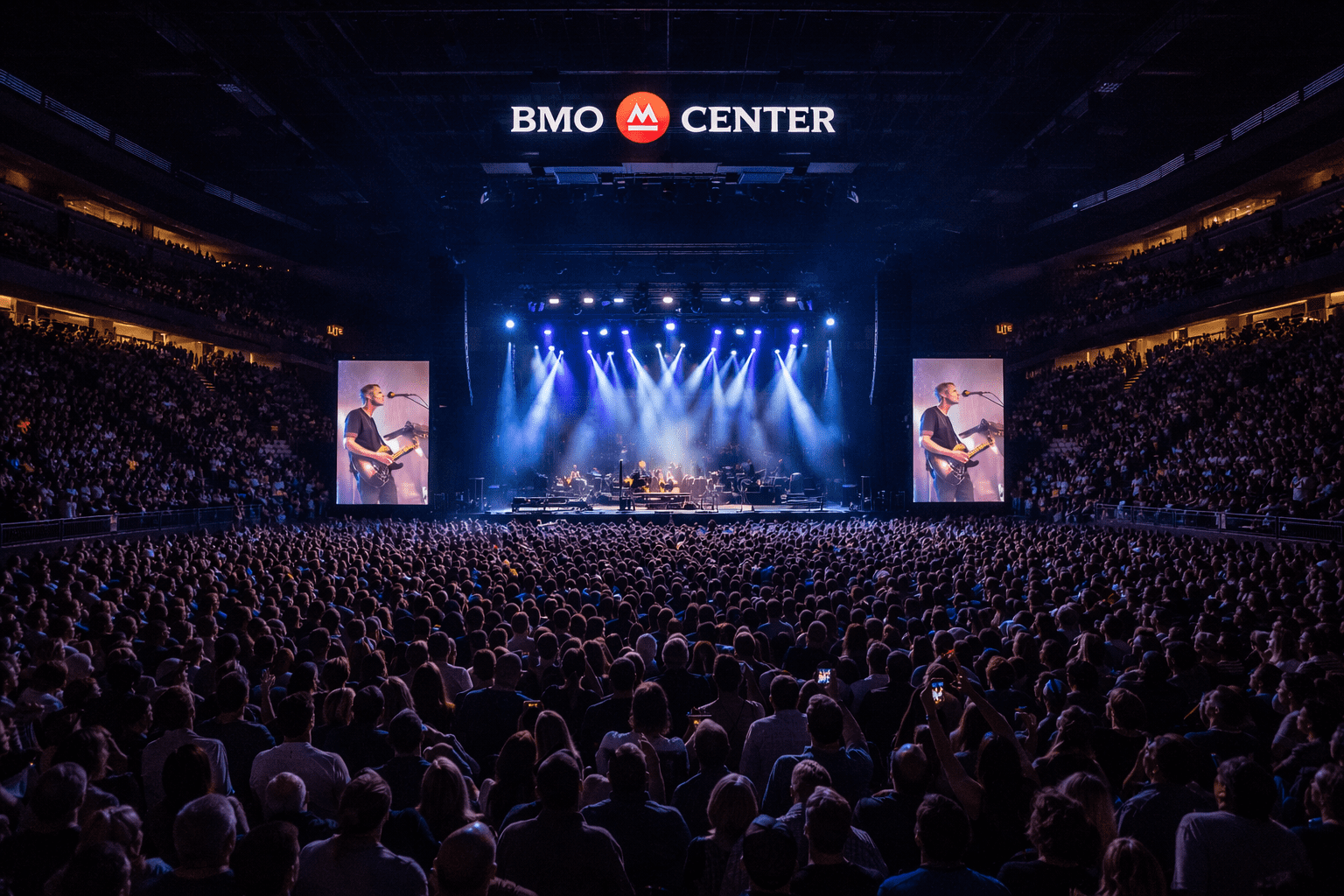 Large crowd at a concert inside BMO Center, facing a brightly lit stage with video screens and overhead logo.