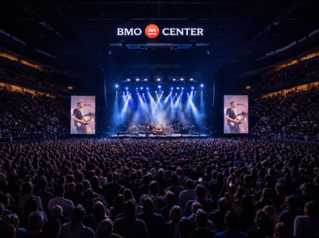 Large crowd at a concert inside BMO Center, facing a brightly lit stage with video screens and overhead logo.