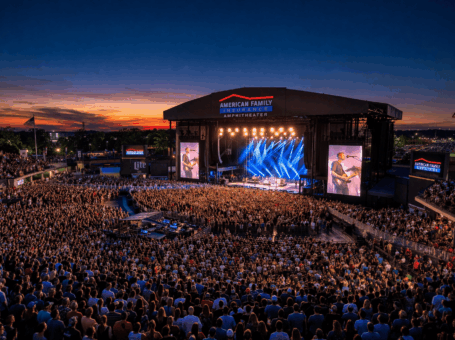 Large crowd at a concert inside the American Family Insurance Amphitheater at dusk, with a brightly lit stage and massive video screens.